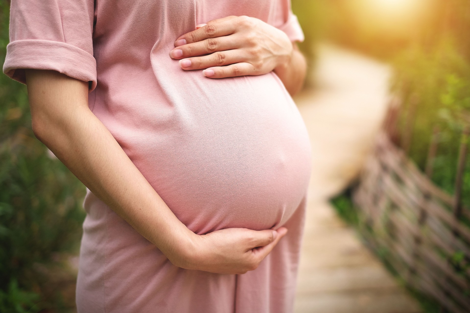 Pregnant woman standing on a wooden walkway on a background of nature, warm weather.
